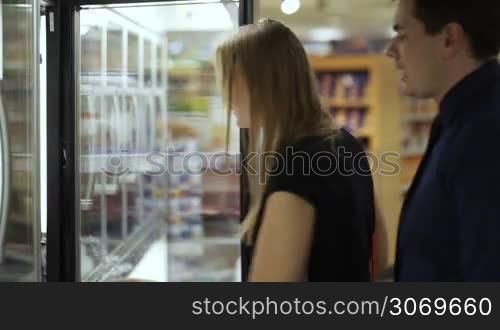 Young couple in frozen section. Woman taking prepack from the fridge, they checking it and leaving