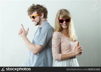Young couple in heart shaped glasses making gun gesture. Friends woman and man having fun.. Couple man and woman making gun gesture.
