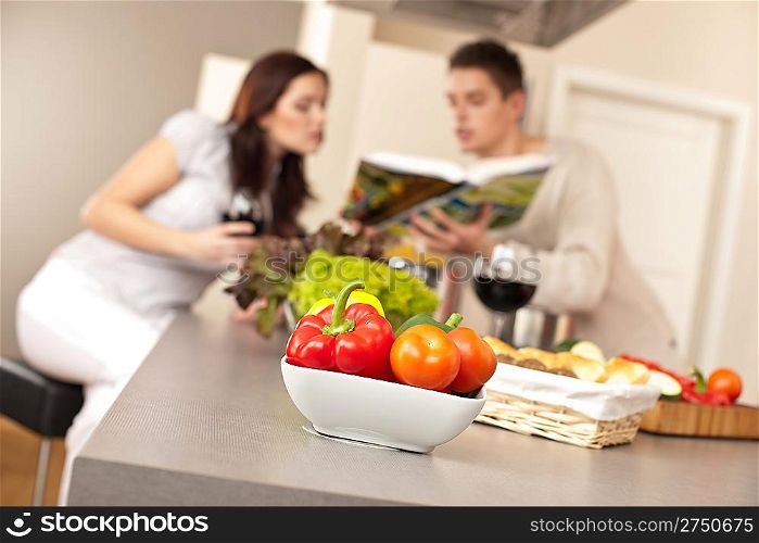 Young couple in kitchen choosing recipe from cookbook drinking red wine