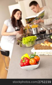 Young couple in kitchen choosing recipe from cookbook drinking red wine