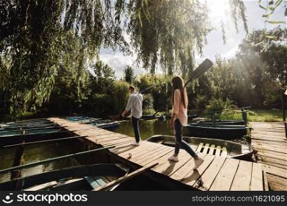 young couple in love having fun with oars on the wooden bridge. stylish woman and man enjoy canoeing on sunny lake. young couple in love having fun with oars on the wooden bridge. stylish woman and man enjoy canoeing on sunny lake.