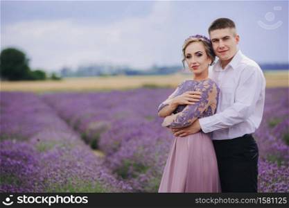Young couple in love hugging and walking in a lavender field on summer day. girl in a luxurious purple dress.. Young couple in love hugging and walking in a lavender field on summer day. girl in a luxurious purple dress