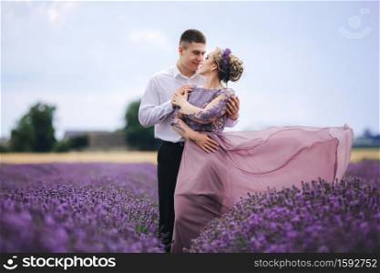 Young couple in love hugging and walking in a lavender field on summer day. girl in a luxurious purple dress and with hairstyle.. Young couple in love hugging and walking in a lavender field on summer day. girl in a luxurious purple dress and with hairstyle
