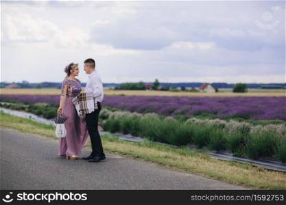 Young couple in love hugging near a lavender field on summer day. girl in a luxurious purple dress and with hairstyle with basket of flowers in hand. Young couple in love hugging near a lavender field on summer day. girl in a luxurious purple dress and with hairstyle with basket of flowers in hand.