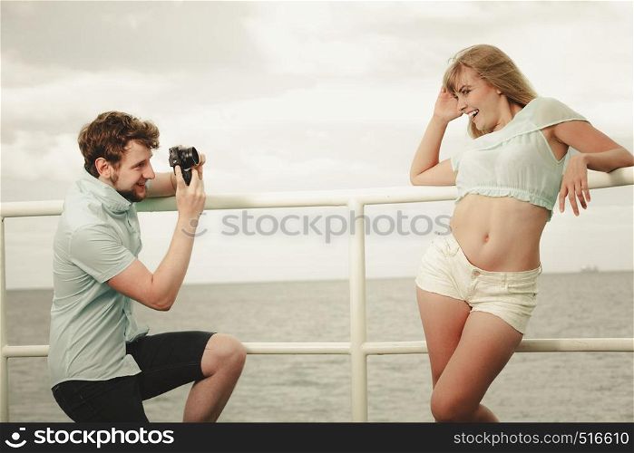 Young couple in love is taking photos on sea pier. Boyfriend photographing his lovely girlfriend outdoor on sea pier