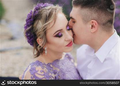 Young couple in love kissing in a lavender field on summer clody day. girl in a luxurious purple dress and with hairstyle.. Young couple in love kissing in a lavender field on summer clody day. girl in a luxurious purple dress and with hairstyle