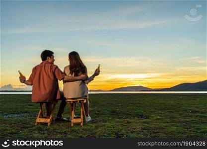 young couple in love sitting and party at the grass filed at sunset