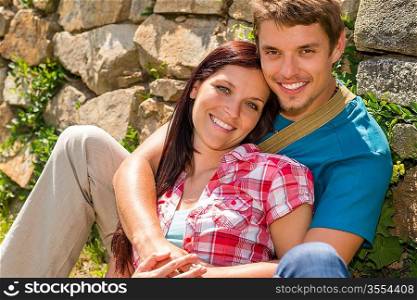 Young couple in love sitting leaning against wall sunny day