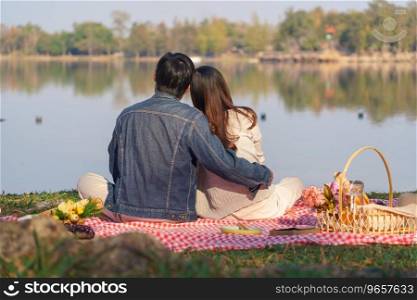 Young couple in love sitting on blanket with picnic basket and embracing to watching lake view.
