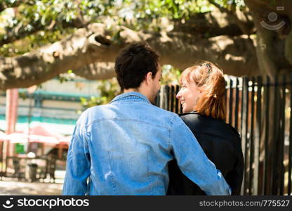 Young couple in love standing with their backs towards camera in a park.