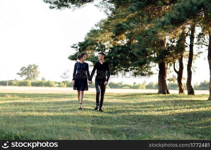 Young couple in love walking in the summer park holding hands. woman and man dressed in black clothes have a date outdoors. Romantic relationship. Valentines Day.. Young couple in love walking in the summer park holding hands. woman and man dressed in black clothes have a date outdoors. Romantic relationship. Valentines Day