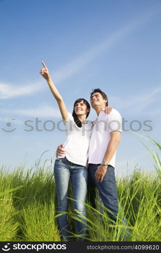 young couple in meadow with hand in air, hugging and smiling. Copy space