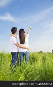 young couple in meadow with hand in air, hugging and smiling. Copy space