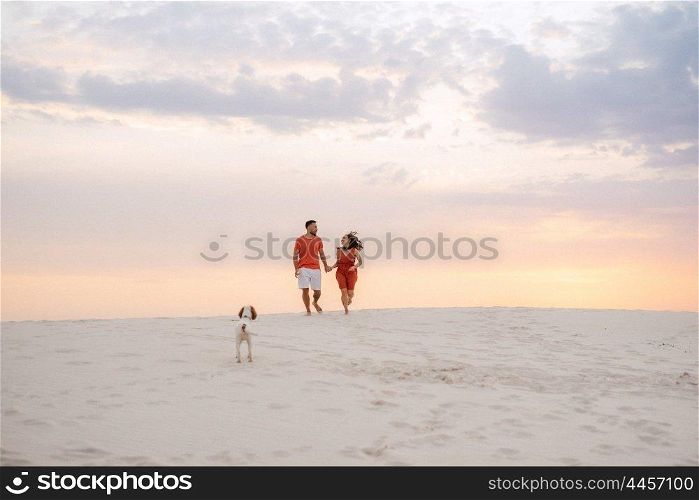 young couple in orange clothes with dog in the desert white sands