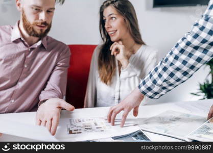 Young couple in talking to real estate agent.  Looking at a model of their new house in real estate agency office.. Real Estate Agency. Couple Looking at a Model of Their New Home 