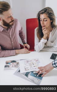 Young couple in talking to real estate agent.  Looking at a model of their new house in real estate agency office.. Real Estate Agency. Couple Looking at a Model of Their New Home 