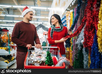 Young couple in the department of holiday decorations in supermarket, family tradition. December shopping. Young couple in department of holiday decorations