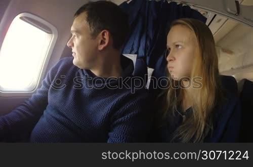 Young couple in the plane. Man being offended and looking out the illuminator, woman teasing him. Then the laughing and making peace