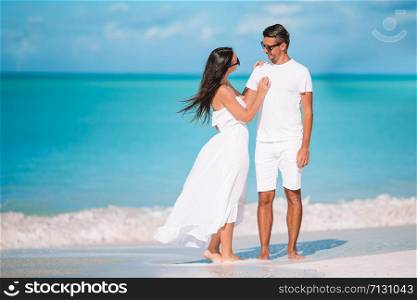 Young couple in white on the beach during summer vacation. Happy lovers enjoy their honeymoon at exotic island. Young couple walking on tropical beach with white sand and turquoise ocean water at Antigua island in Caribbean