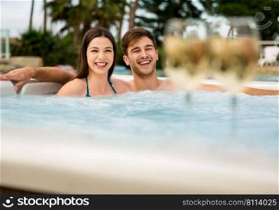 Young couple inside a hot tube and tasting wine