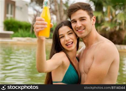 Young couple inside the pool and drinking natural juices