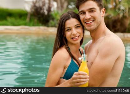 Young couple inside the pool and drinking natural juices
