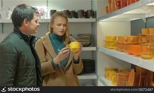 Young couple is choosing cups in utensils shop, there is a wide choice.