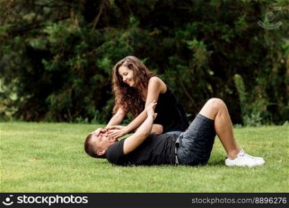 young couple is having fun and playing on the grass on summer day. woman lying over her lover, smiling.. young couple is having fun and playing on the grass on summer day. woman lying over her lover, smiling