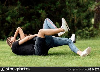 young couple is having fun and playing on the grass on summer day. woman lying over her lover, smiling.. young couple is having fun and playing on the grass on summer day. woman lying over her lover, smiling