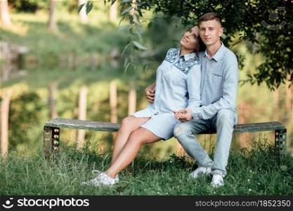 Young couple is hugging and sitting near the lake on sunny day. Man and woman on summer holiday. Concept of lovely family. selective focus.. Young couple is hugging and sitting near the lake on sunny day. Man and woman on summer holiday. Concept of lovely family. selective focus