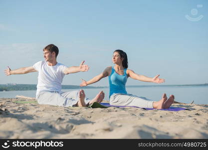 Young couple is practicing yoga at beach