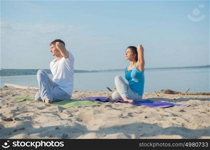 Young couple is practicing yoga at beach