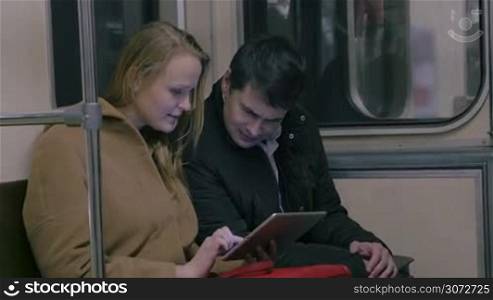 Young couple is sitting in metro train and passing time with tablet PC.