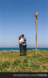 Young couple kissing embraced by a direction sign on the coast. Couple kissing embraced by a direction sign
