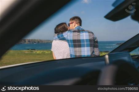 young couple kissing viewed from inside a car near the coast. Young couple kissing near the coast