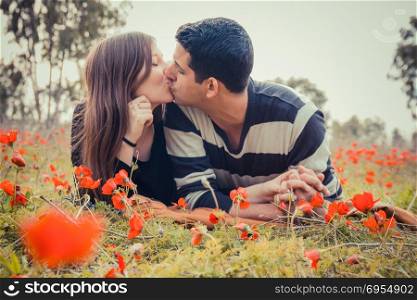 Young couple kissing while lying on the grass in a field of red poppies.