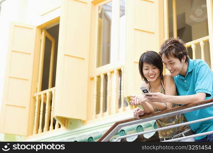 Young couple leaning against a railing and looking at a mobile phone