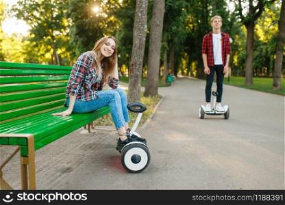 Young couple leisures with gyro board in summer park. Outdoor recreation with electric gyroboard. Transport with balance technology. Couple leisures with gyro board in summer park
