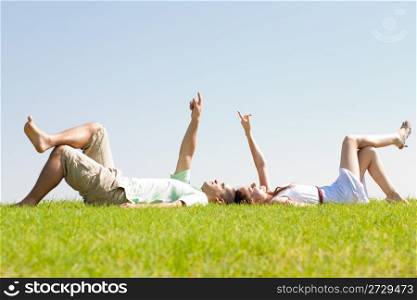 young couple lie down on grass and point to the sky, outdoor at park