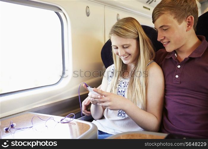 Young Couple Listening To Music On Train Journey