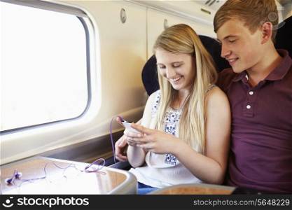 Young Couple Listening To Music On Train Journey