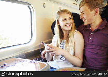 Young Couple Listening To Music On Train Journey