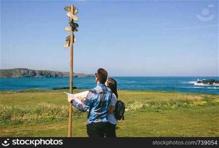 Young couple looking a map and direction sign near the coast. Couple looking a map and direction sign