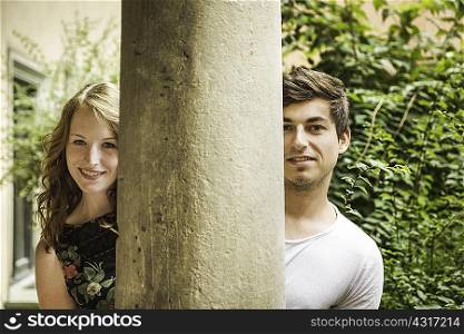 Young couple looking around pillar
