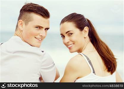 Young couple looking at camera while sitting next to each other on beach. Young couple looking at camera while sitting next to each other on beach in sports wear