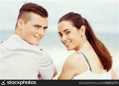 Young couple looking at camera while sitting next to each other on beach. Young couple looking at camera while sitting next to each other on beach in sports wear