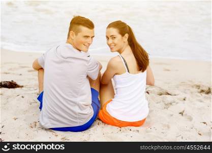 Young couple looking at camera while sitting on beach. Young couple looking at camera while sitting together on beach