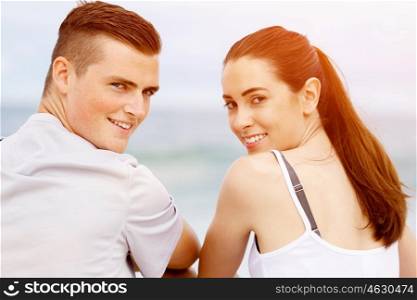 Young couple looking at camera while sitting on beach. Young couple looking at camera while sitting together on beach