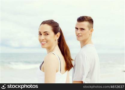 Young couple looking at camera while standing next to each other on beach. Young couple looking at camera while standing next to each other on beach in sports wear