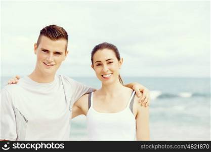 Young couple looking at camera while standing next to each other on beach. Young couple looking at camera while standing next to each other on beach in sports wear